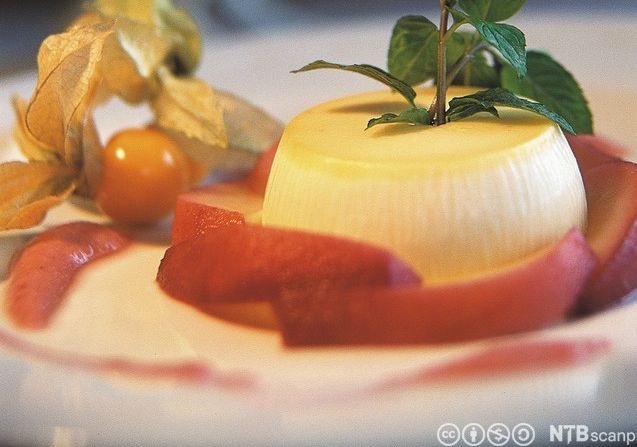 Råmjølkspudding på ei skål, pynta med eit grønt blad og physalis. Foto.