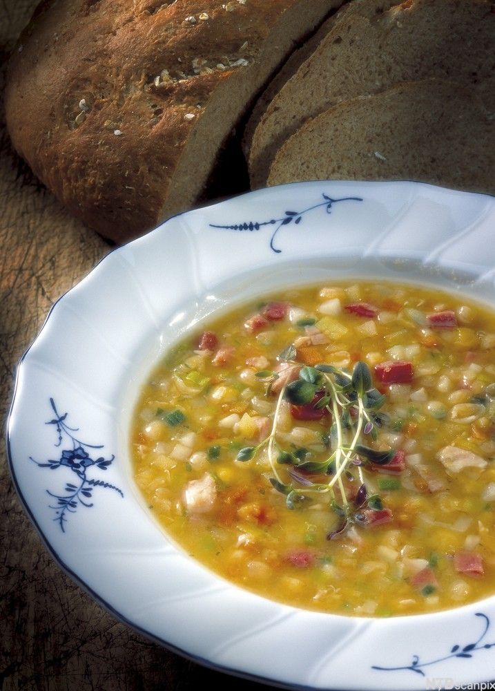 Gul ertersuppe med kjøttbiter i. Ved siden av tallerkenen ligger to brødskiver. Foto.
