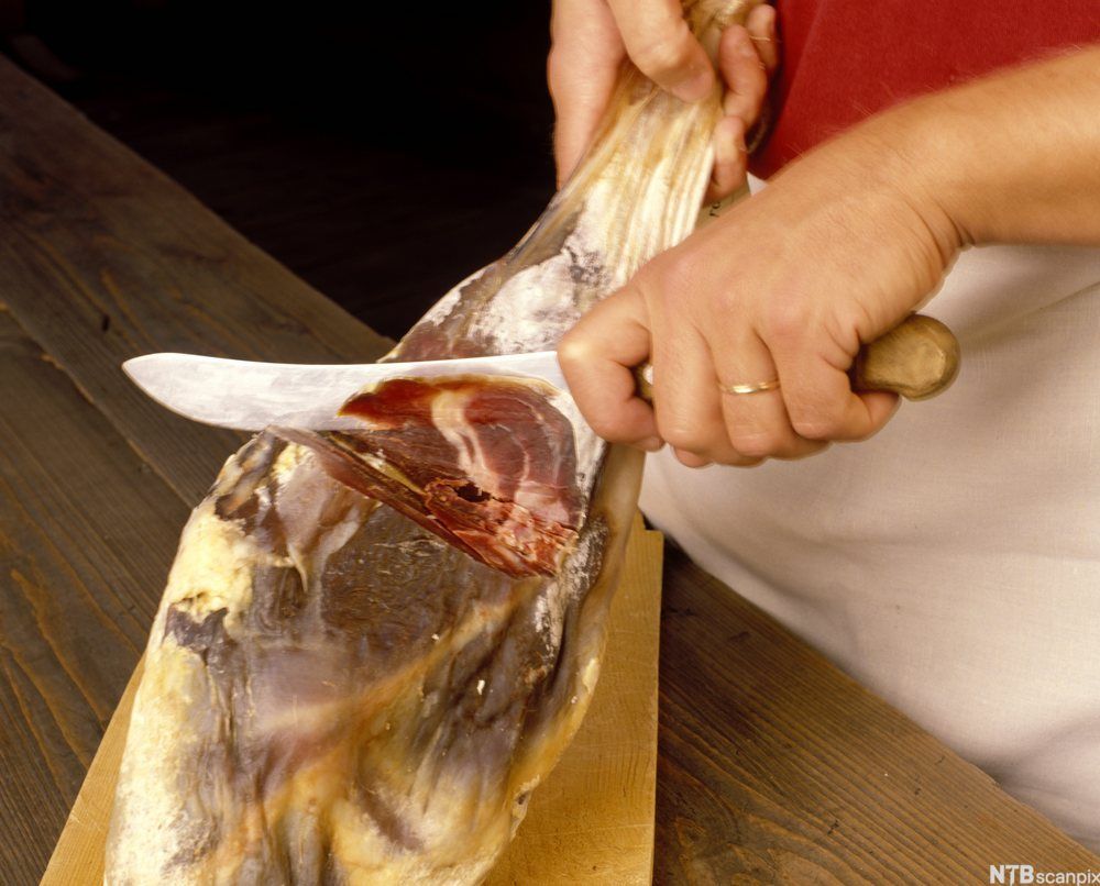 Et fenalår blir skjært opp med en kniv. Foto.