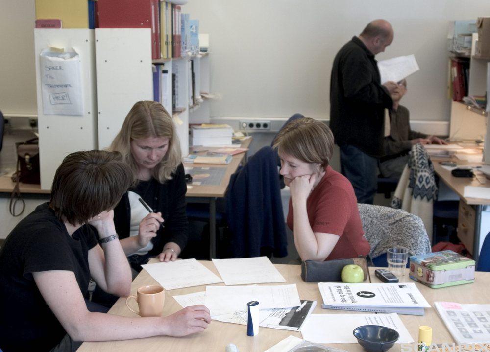 Tre voksne som samarbeider rundt et bord. Foto.