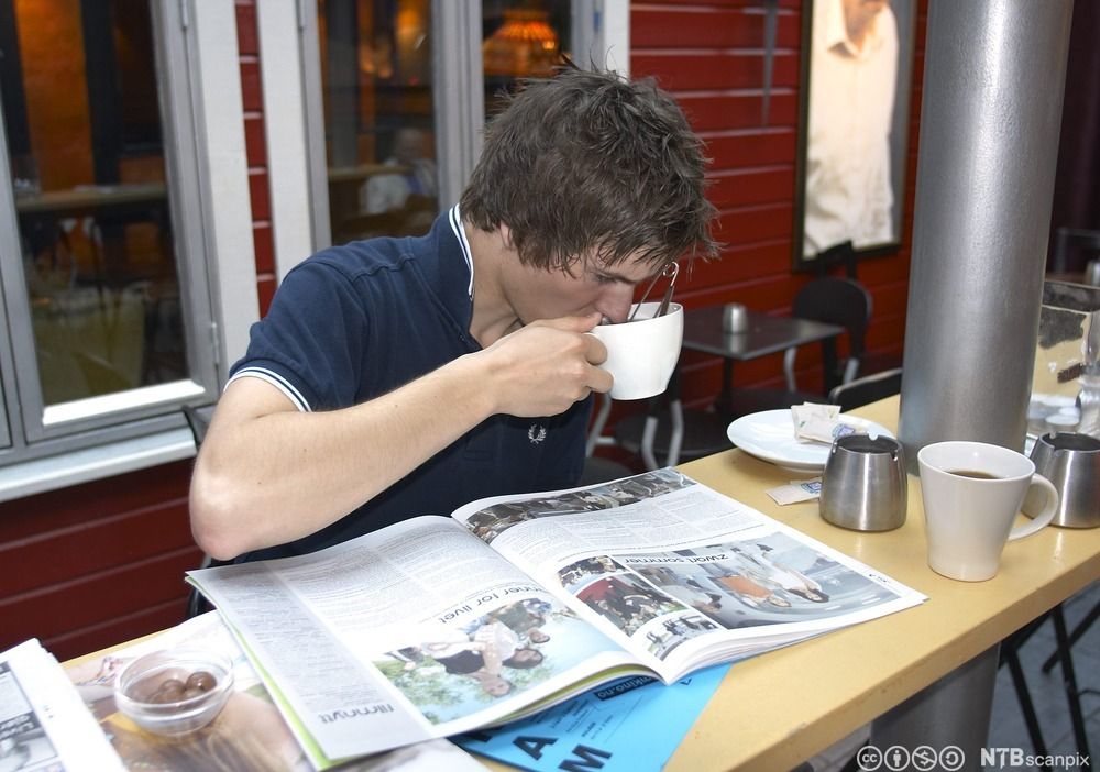 Ung gutt leser avis på kafé. Foto. 
