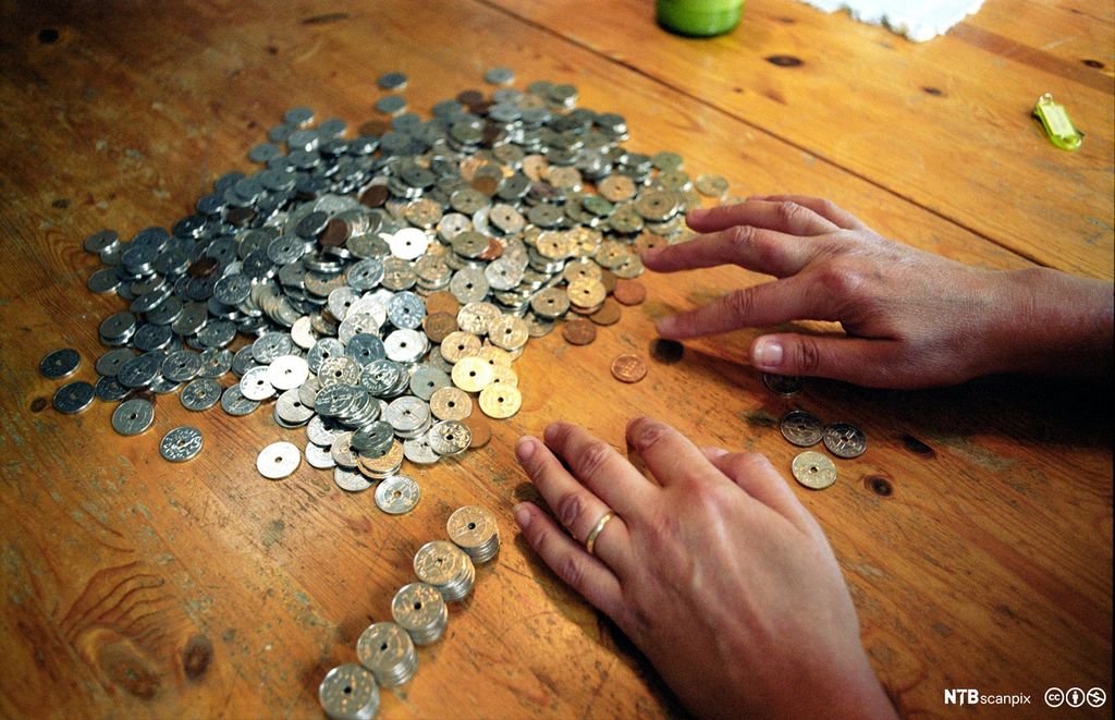 Person sorterer kronestykke og 50-ørar. På bordet er det hundrevis av myntar, nokre av dei er stabla. Foto.