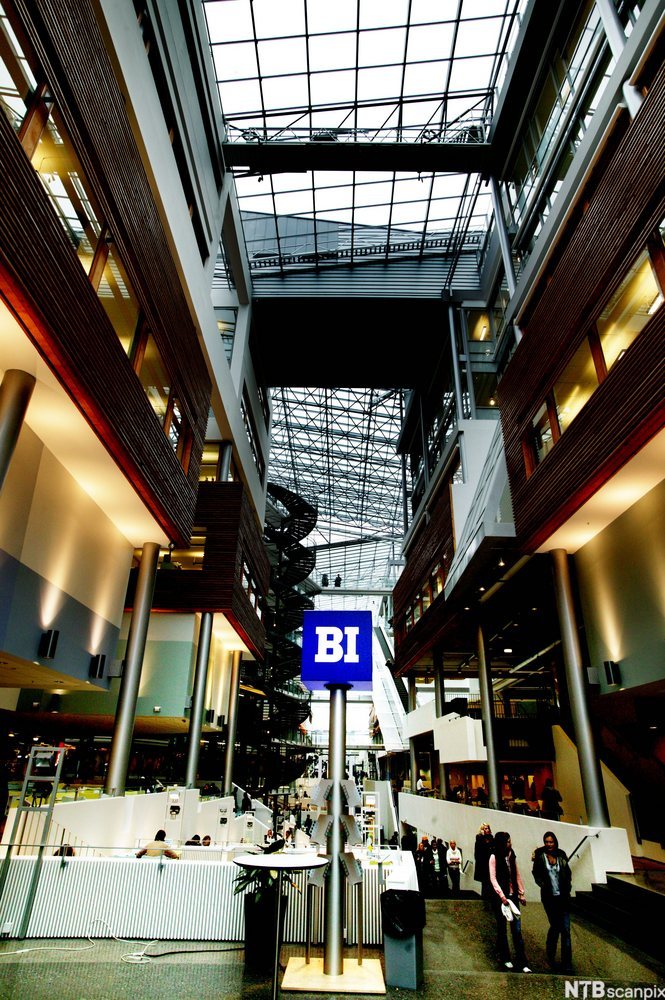 Mennesker i et innendørs fellesareal. På et blått skilt står det BI med hvite bokstaver. Foto.