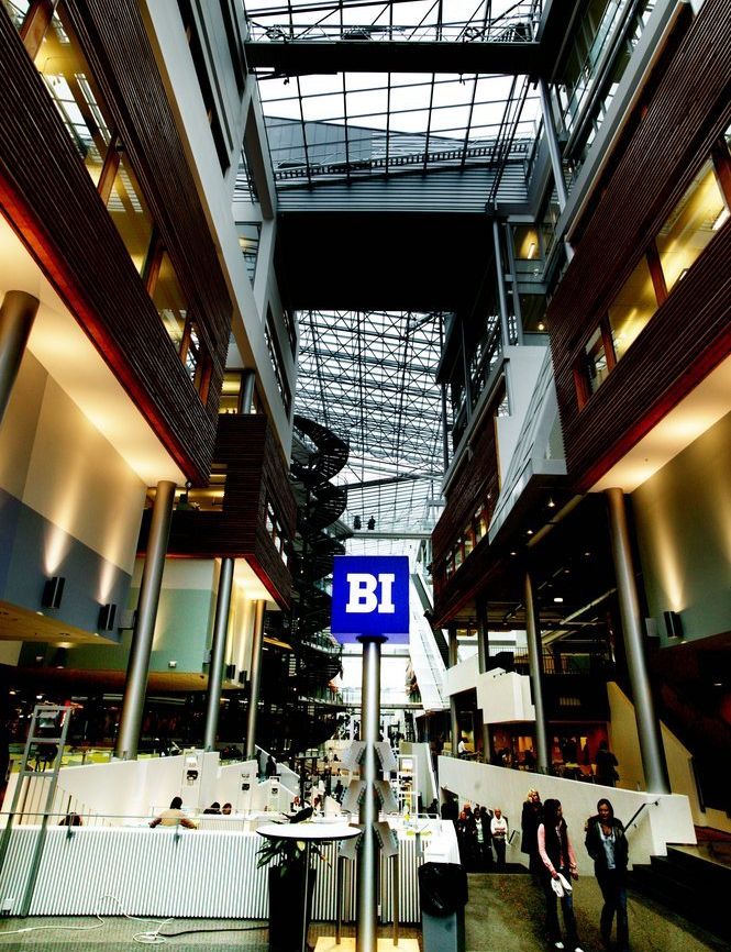 Mennesker i et innendørs fellesareal. På et blått skilt står det BI med hvite bokstaver. Foto.