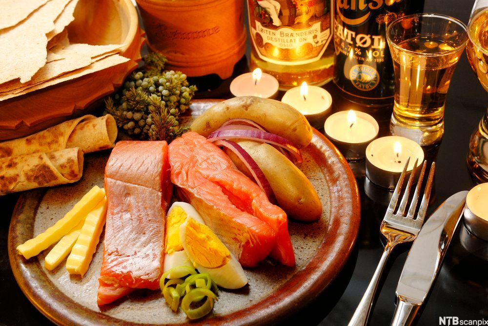 Rakfisk anrettet på tallerken med løk, egg, poteter, smør, lefse, flatbrød, rømme, purre, øl og akevitt. Foto.