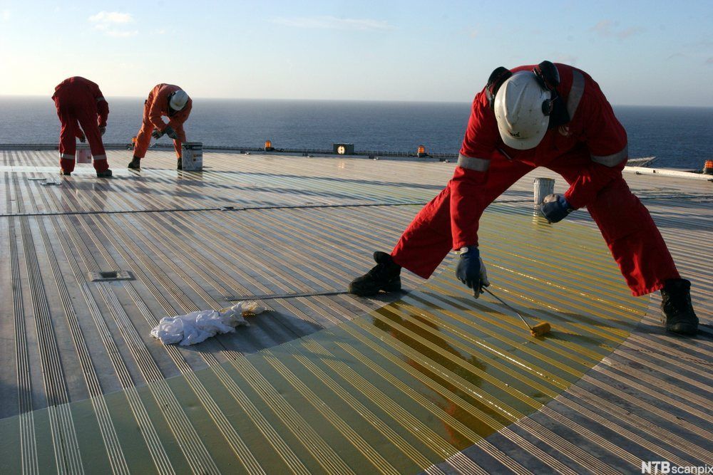 Tre arbeidere maler et landingsdekk for helikopter. Foto.