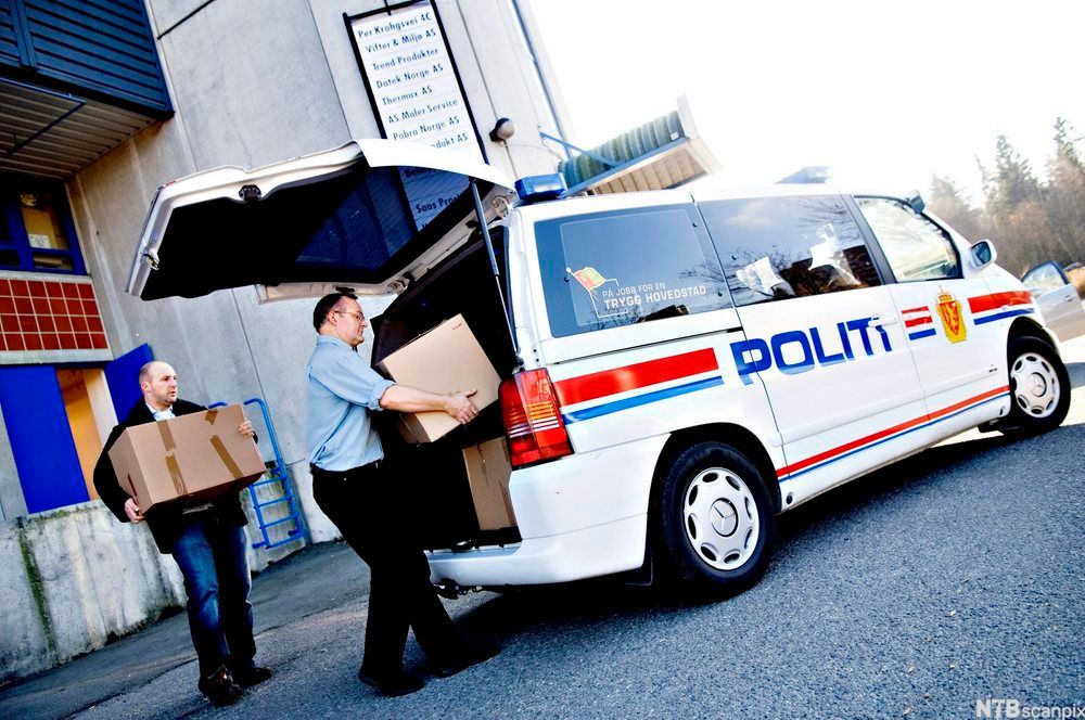 To menn bærer pappkasser inn i en politibil. Foto.