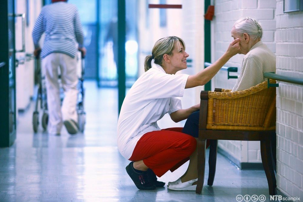 Pleier snakker med beboer og stryker henne på kinnet. Foto.