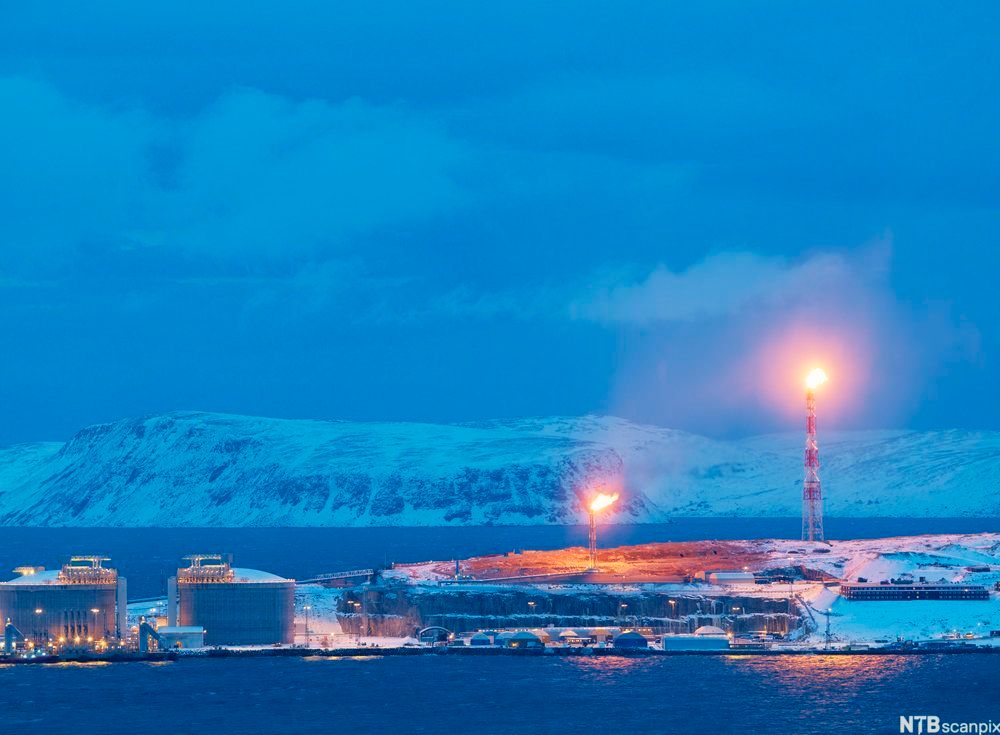 LNG-anlegg med små og store bygninger og to høye tårn med gassflammer. Foto.