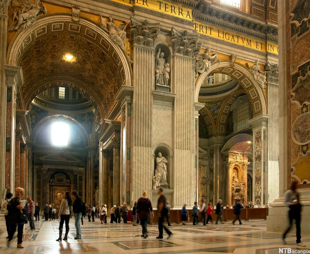 Høye bueåpninger og barokke utsmykninger inne i kirkerommet. Foto.