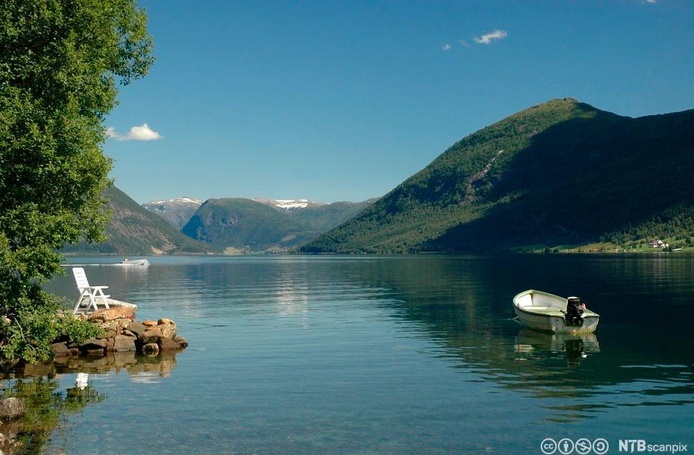 Småbåt som har ankra opp i fjordlandskap. Foto.