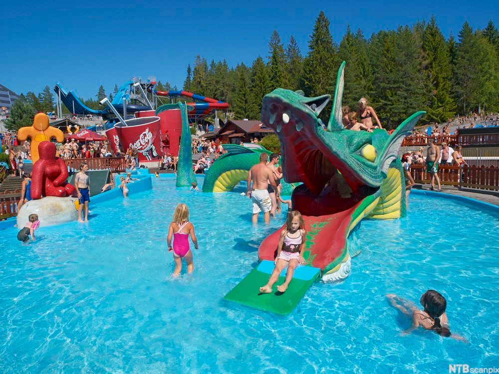 Fra badelandet og vannparken i Bø Sommarland. I et stort basseng koser både barn og voksne seg på og ved en vannsklie formet som et dragehode. Foto.