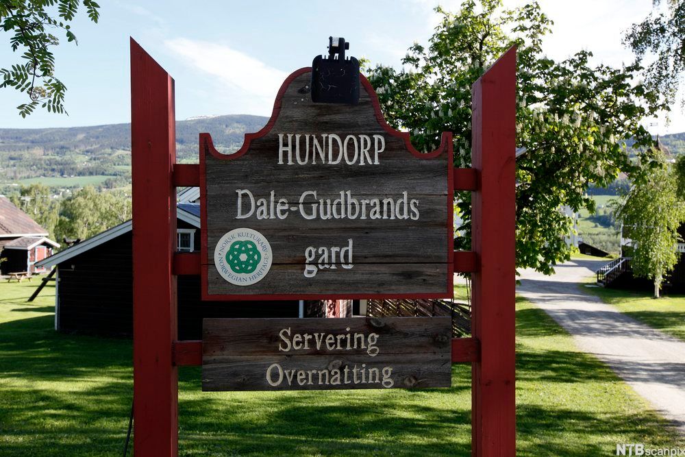 Bilde av Dale-Gudbrands gård. På et treskilt står navnet på gården, at de har servering og overnatting, og et merke for norsk kulturarv. Foto.