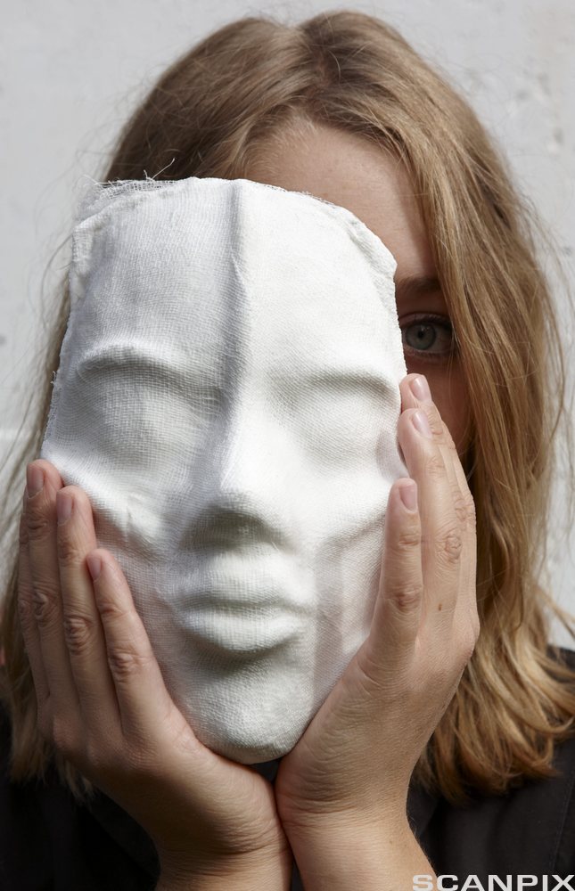 Jente som holder en maske delvis foran ansiktet. Foto.
