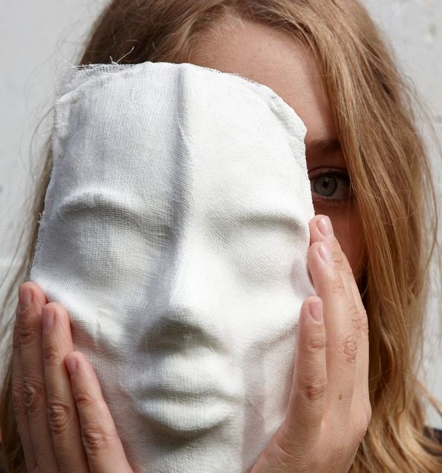 Jente som held ei maske delvis framfor ansiktet. Foto.
