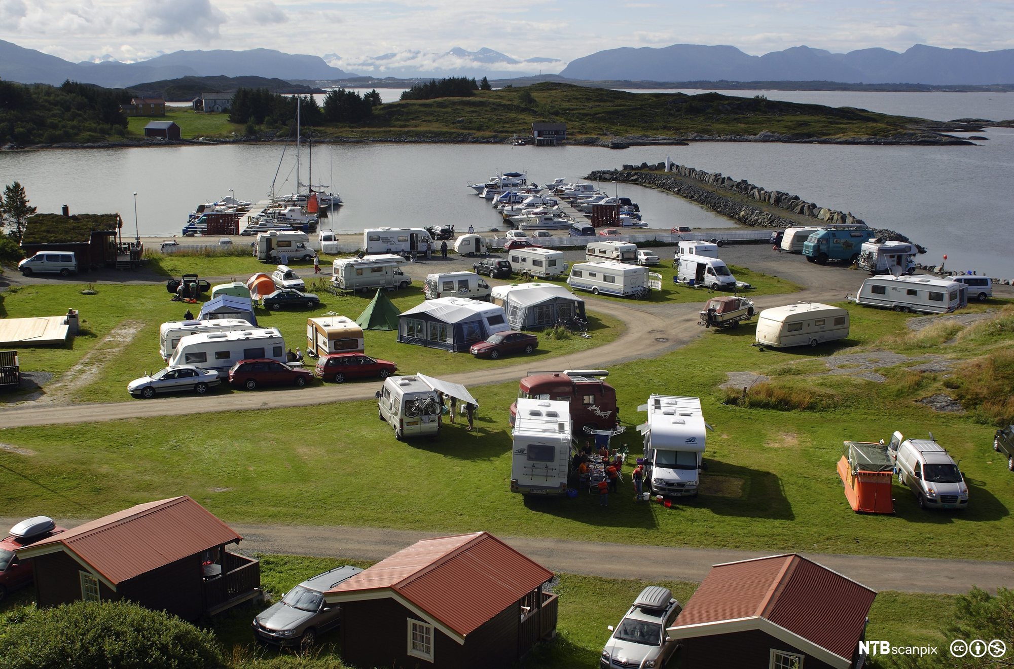 Oversiktsbilde som viser en campingplass med telt, bobiler, utleiehytter og båthavn. Foto.