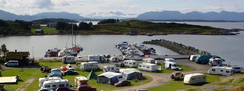 Oversiktsbilde som viser en campingplass med telt, bobiler, utleiehytter og båthavn. Foto.