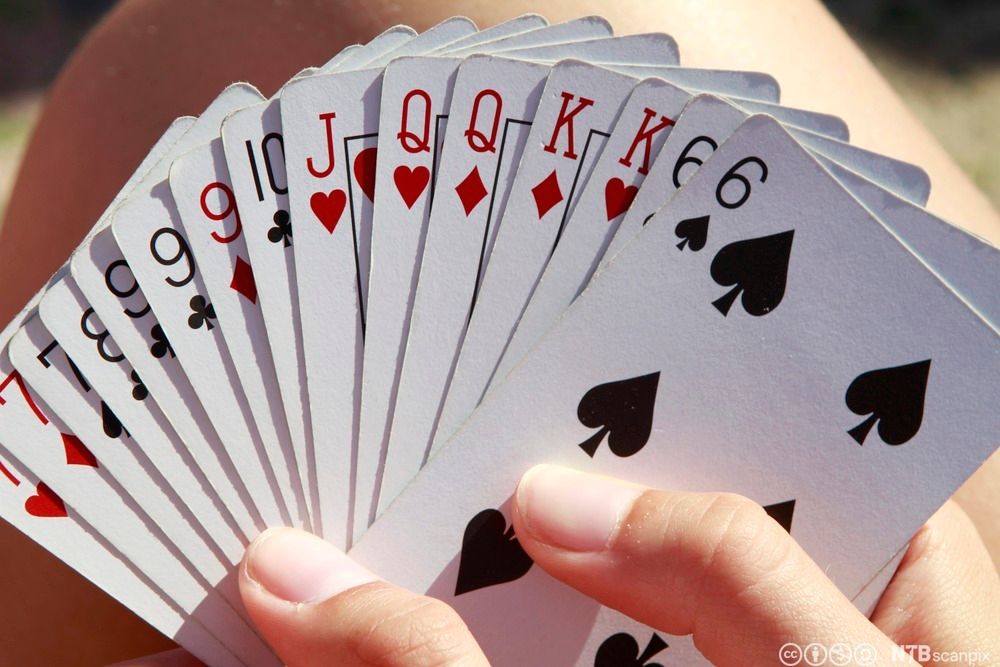 Hender som holder spillkort i ulike farger og valører. Foto.