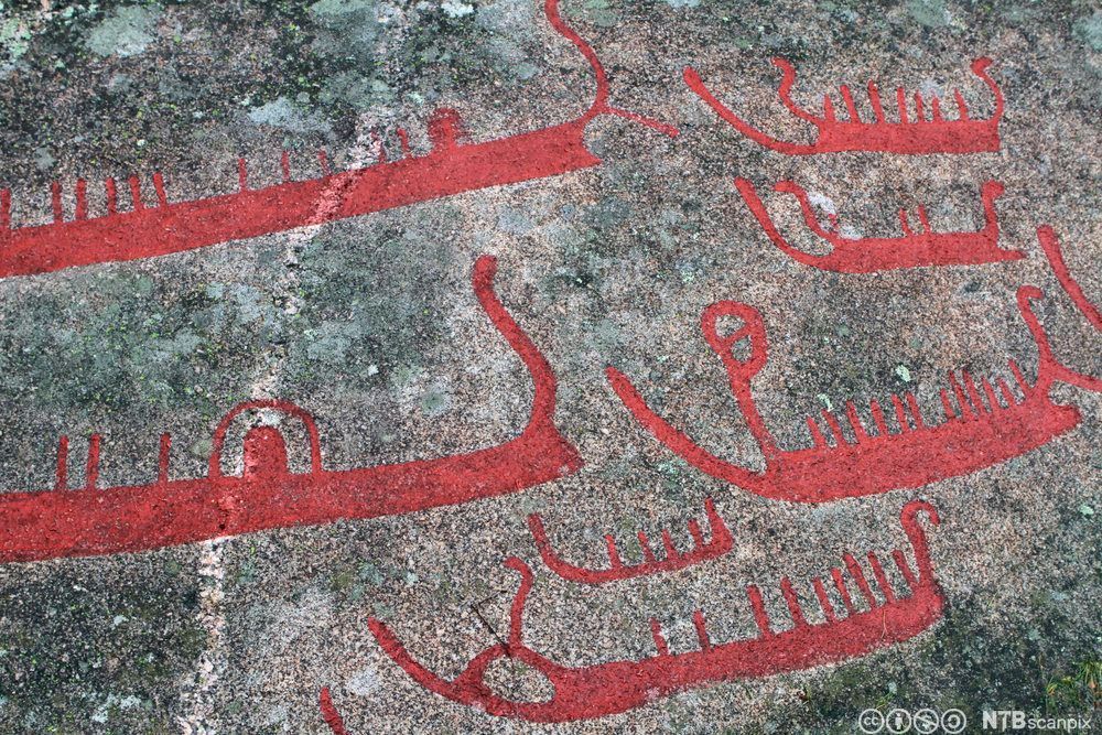 Helleristninger av stiliserte båter med vertikale streker om bord. Foto. 