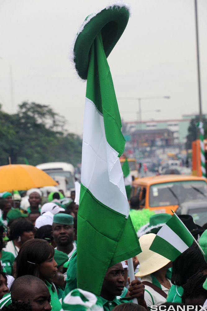 A man raises the Nigerian flag during a street procession marking the 51st independence celebration