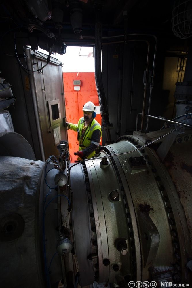 En mann åpner døra til et maskinrom der det er en gassturbin. Foto. 