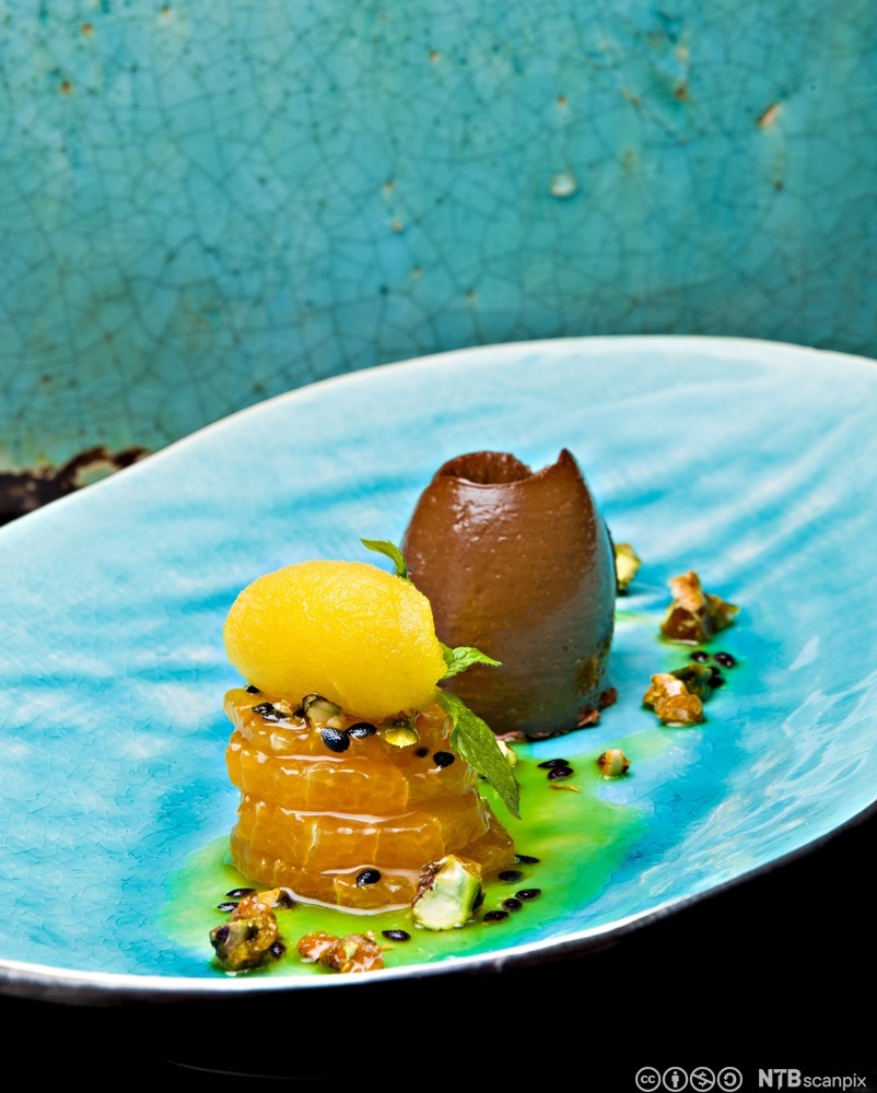 Dessert i sterke fargar og kreative former lagt på ein havblå tallerken. Foto.