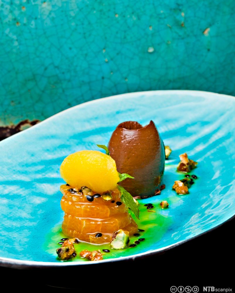 Dessert i sterke farger og kreative former anrettet på en havblå tallerken. Foto.