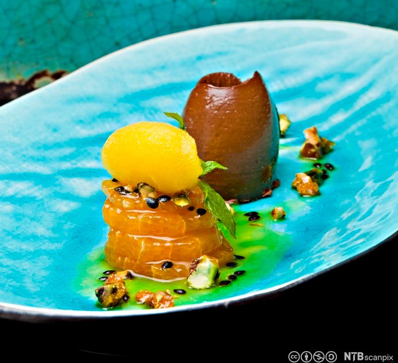 Dessert i sterke fargar og kreative former lagt på ein havblå tallerken. Foto.