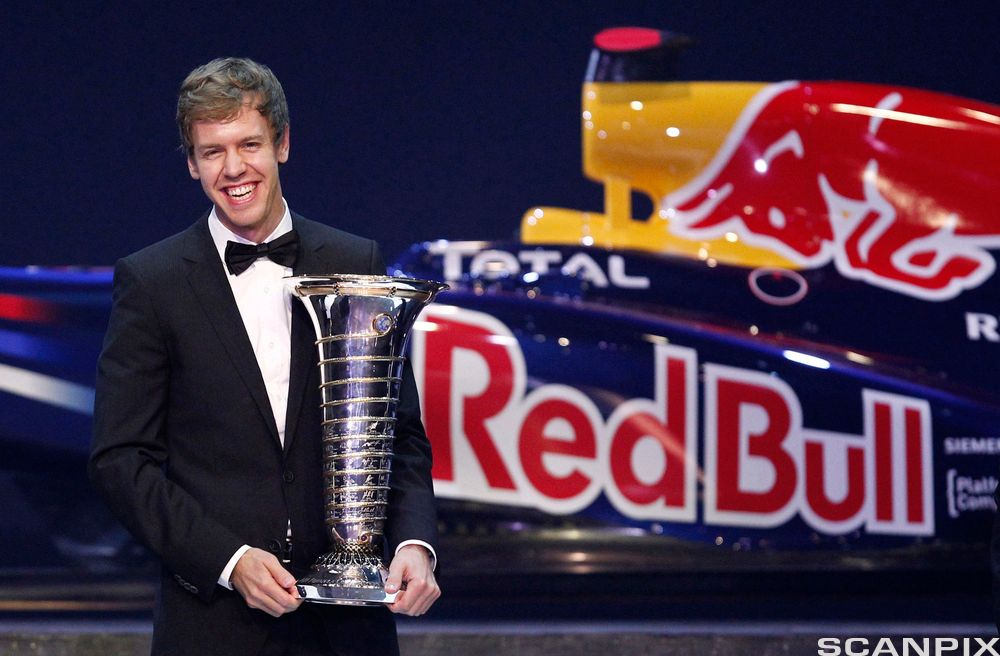 Reklame for Red Bull bak en mann i smoking som holder en pokal. Foto.
