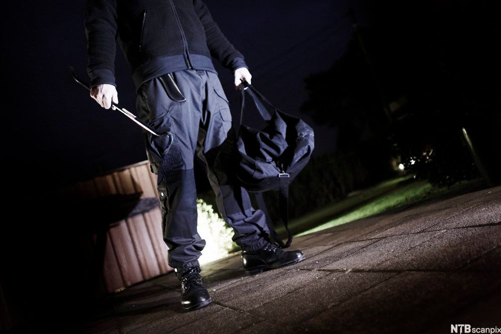 Innbruddstyv som bærer på bag og brekkjern. Det er mørkt.