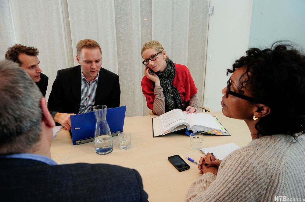 Fem personar sit i eit kontormøte. Foto.