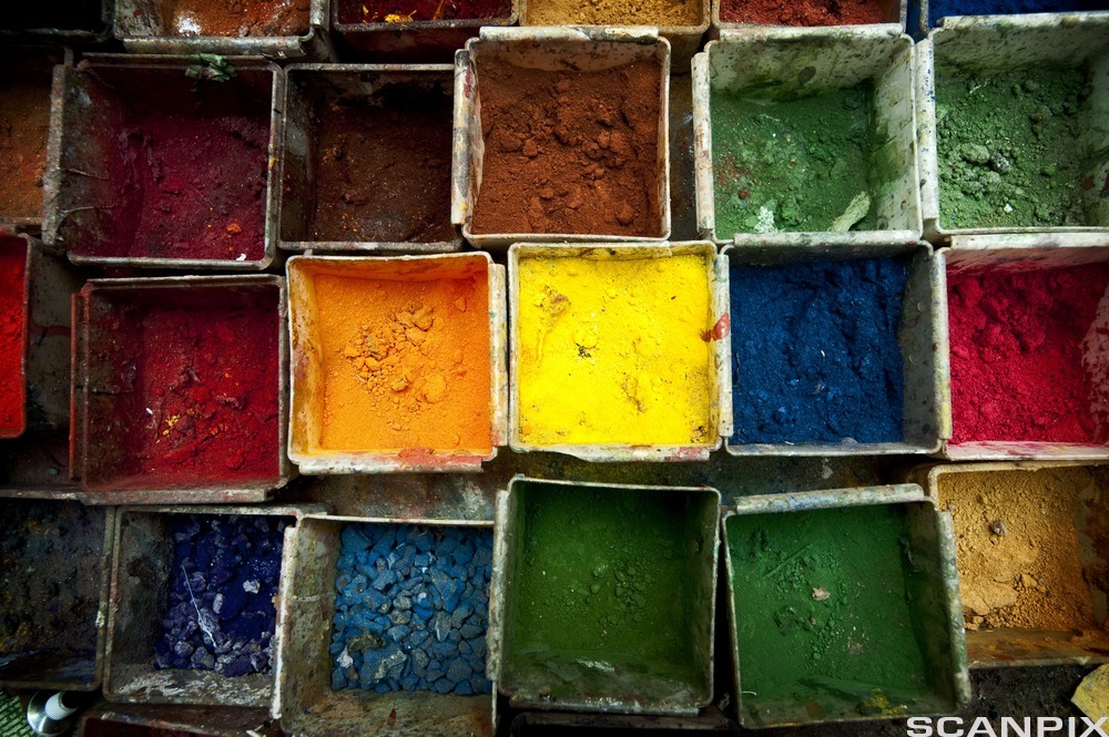 Åpne bokser fylt med hver sine fargerike pigmenter, blant annet  rødt, oransje, gult, grønt, blått og brunt. Foto.