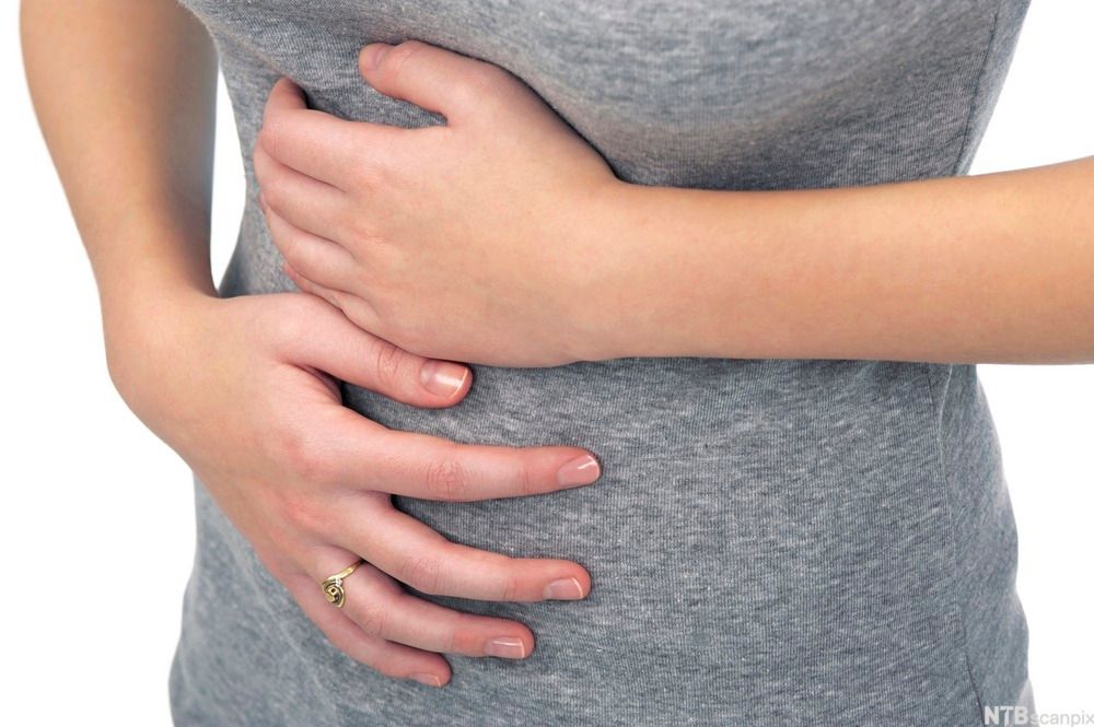 Ei kvinne held hendene på magen. Foto.