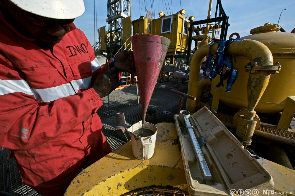 Offshore-arbeider holder en trakt som det renner slam ut av. Slammet renner ut i en liten kanne. Foto.