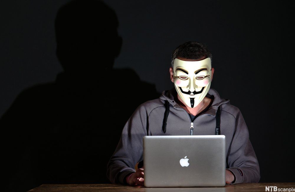 Bilde. Mann med maske foran en dataskjerm.