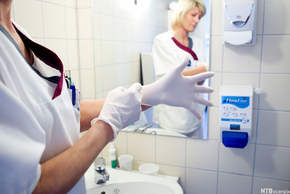 Helsefagarbeider tar på seg engangshansker. Foto.