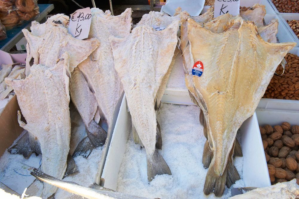 Utspilt tørrfisk på et marked. Det står pris i euro, og ved siden av er det valnøtter, mandler og andre nøtter i løsvekt. Foto. 