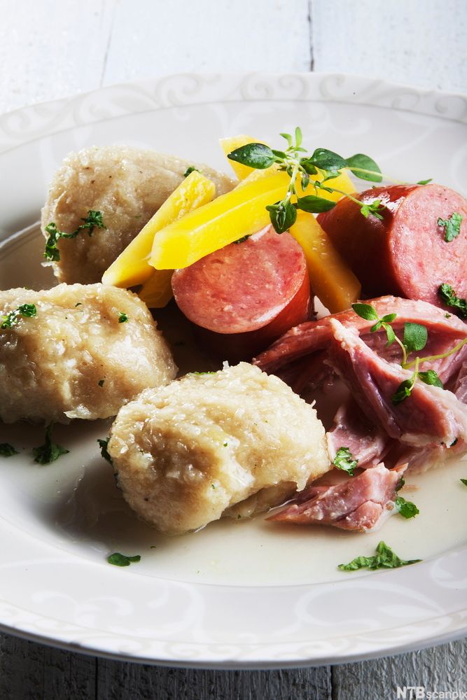 Raspeball med røykt svineknoke, vossakorv og staver av kålrabi på en tallerken. Foto.