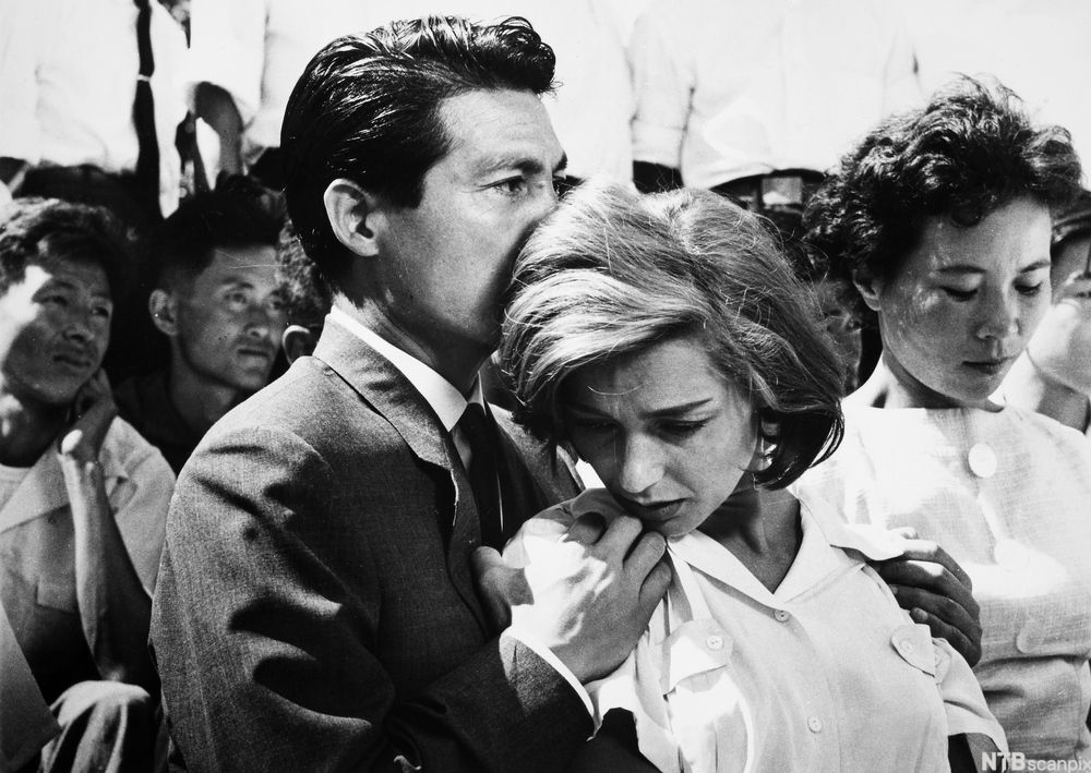 Mann holder rundt en dame i en folkemengde. Svart-hvitt foto.