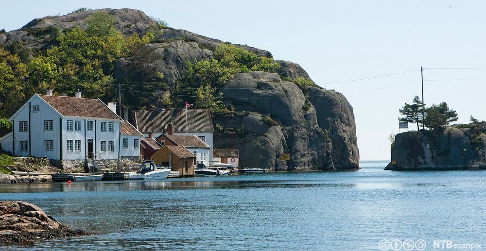 Hvit trehusbebyggelse og sjøhus og et smalt sund. Foto.
