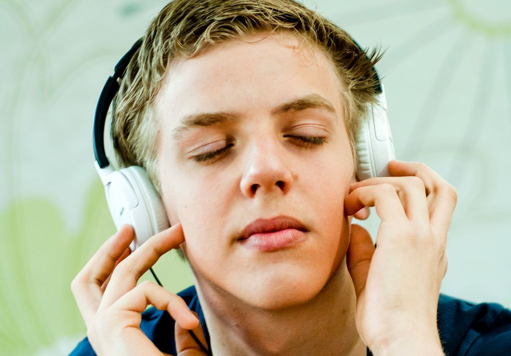 Foto av gut med øyretelefonar og lukka auge.