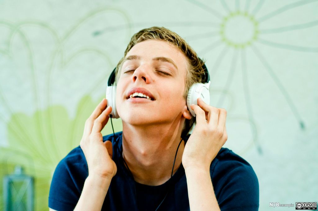 Gut som lyttar til musikk. Han bruker hovudtelefonar og ser ut til å nyte musikken. Foto.