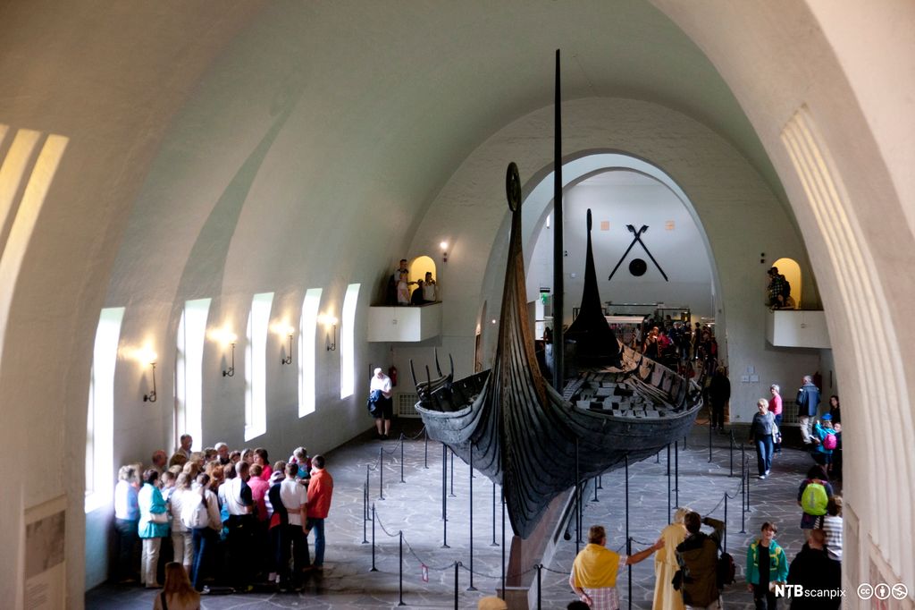 Turister ser på Osebergskipet i samlingen til Vikingskipshuset på Bygdøy i Oslo. Foto.