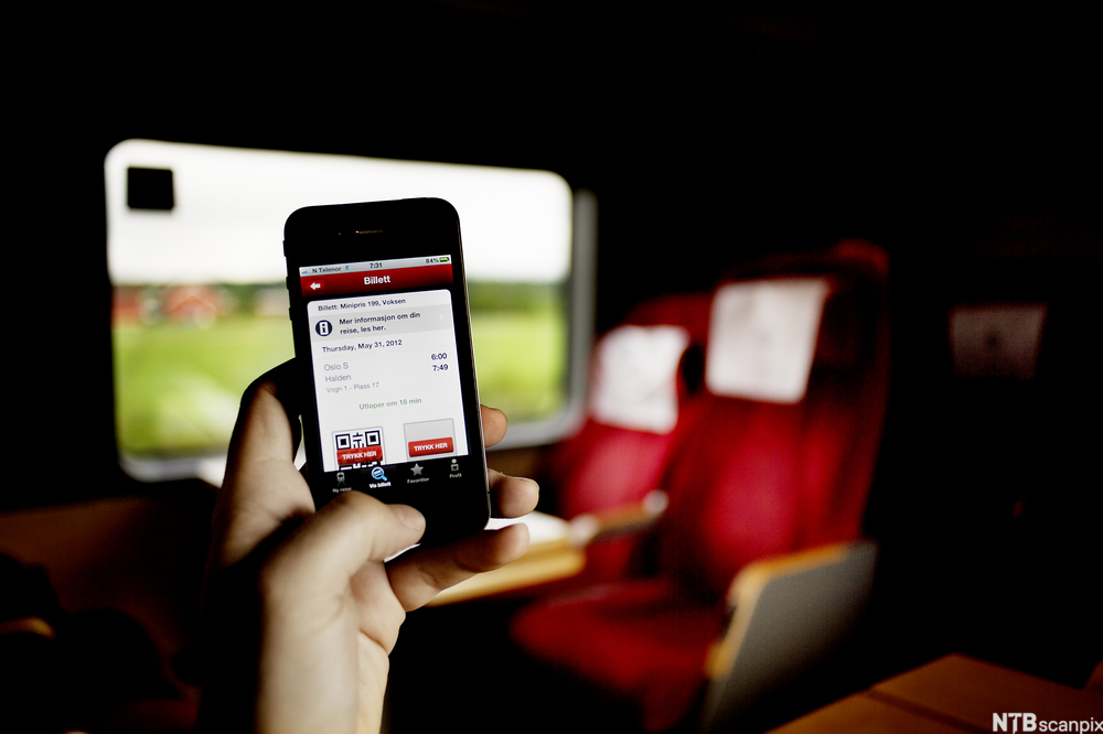 Telefonskjerm som viser elektronisk togbillett. Interiøret i en sittekupé vises i bakgrunnen. Foto.
