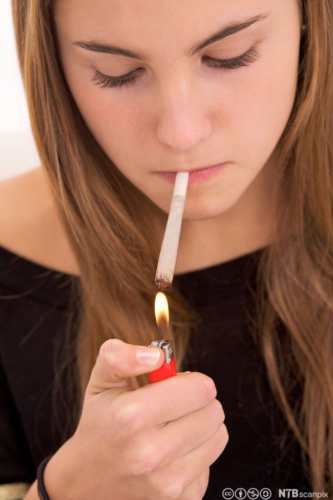 Jente tenner på en joint med en rød lighter. Foto.