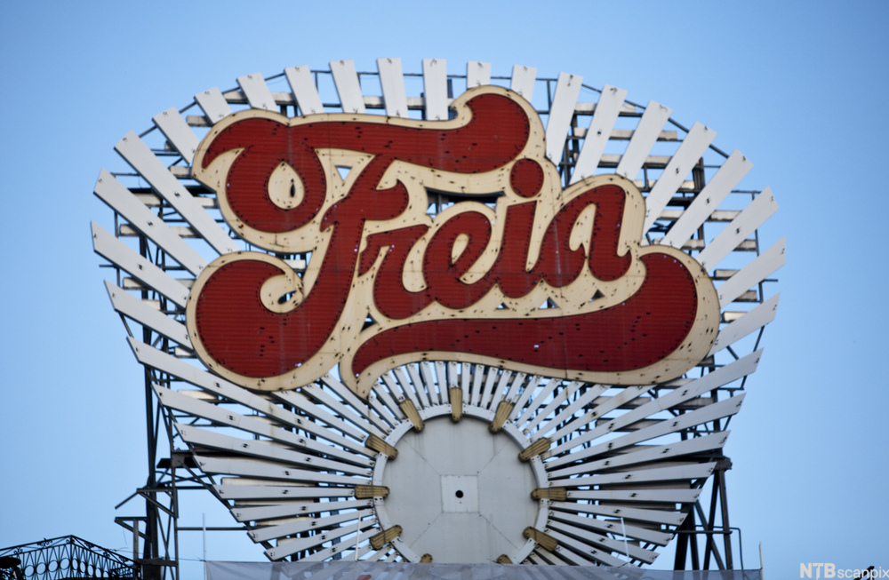 Et Freia-skilt. Det er i rødt og beige og rager i høyden på et bygg. Foto.