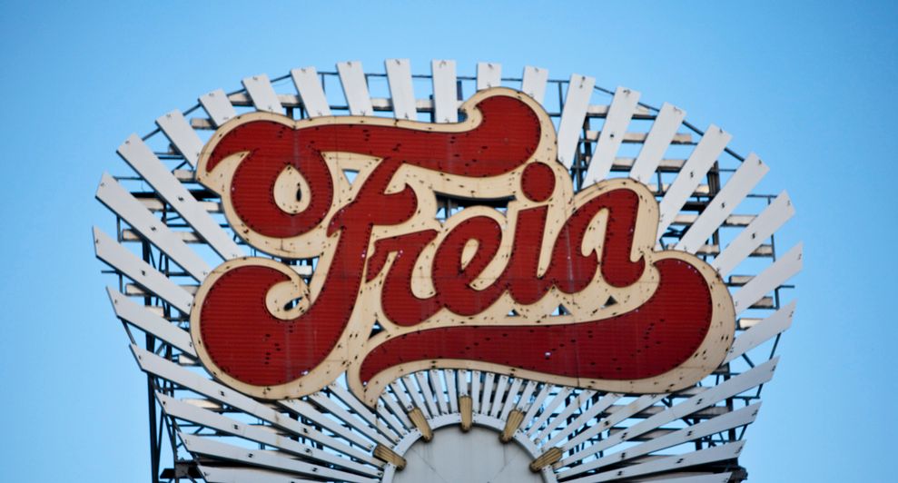 Et Freia-skilt. Det er i rødt og beige og rager i høyden på et bygg. Foto.