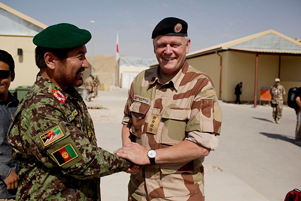 Ein afghansk og ein norsk offiser i kamuflasjeuniformar tek kvarandre smilande i handa i ein militærleir i Afghanistan. Foto.