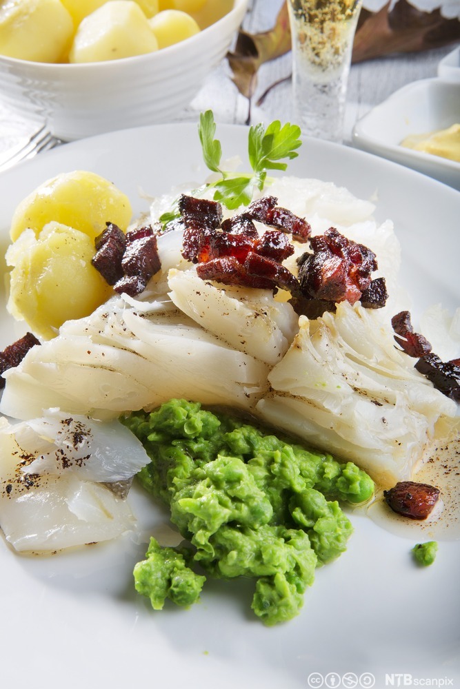Lutefisk og grønn ertepuré anrettet på hvit en tallerken. Foto.