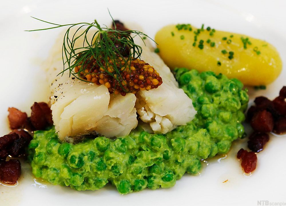 En tallerken med lutefisk, poteter, ertestuing og stekt bacon. Foto.